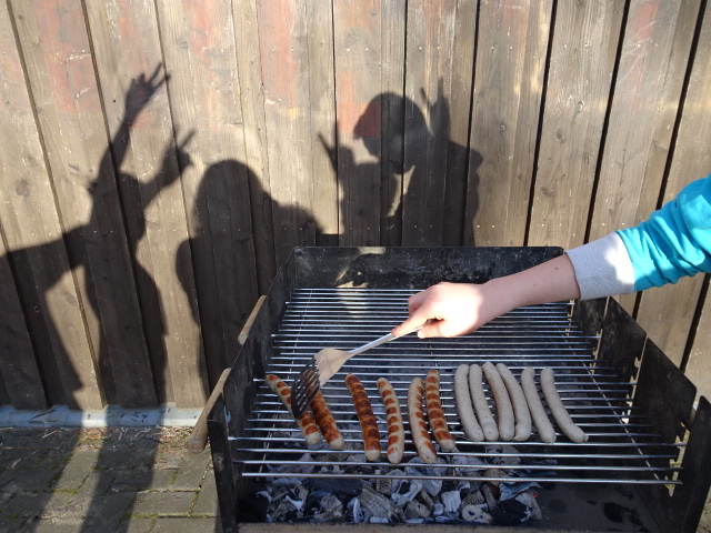 Ein Bild von einem Grill mit Bratwurst, an der Wand da hinter Kinderschatten